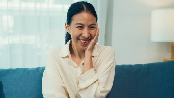 istock Beautiful Asian young woman on sofa click remote controller change channel on television choose favorite comedy or sitcoms in streaming online VOD, video on demand at home. 1449425163