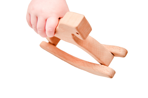 Baby hand and toy wooden rocking horse, close-up, isolated on a white background. Children fingers and an object on a white background