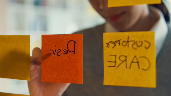 Asian girl focus on transparent board writing roadmap planning on sticky note work outside office in co-working room. Business Woman happy working at co-working space. Alternatives workspace concept.