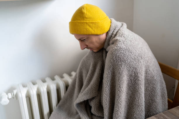 istock Dissatisfied middle aged man having problem with central heating, sitting on chair at home, freezing. Freezing man warm blankets looking at camera while sitting on chair in cold kitchen 1449426800