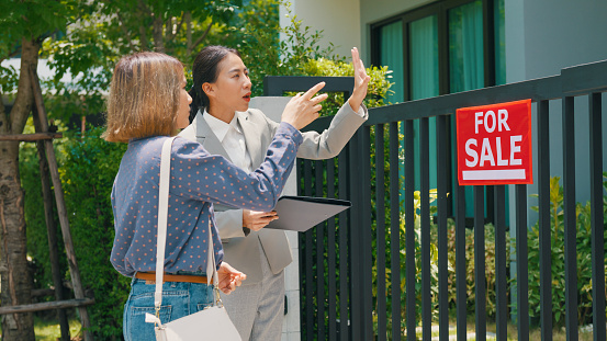 Young Asian woman real estate broker showing house to female buyers outside at home. Buying a new house concept.