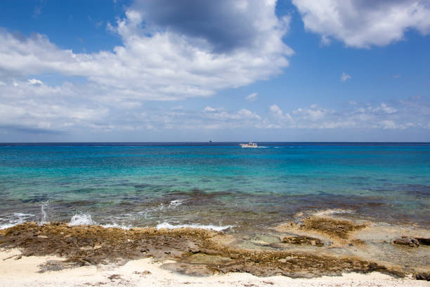 Wave splashes on Cozumel island rocky beach and a boat passing by in a background (Mexico).