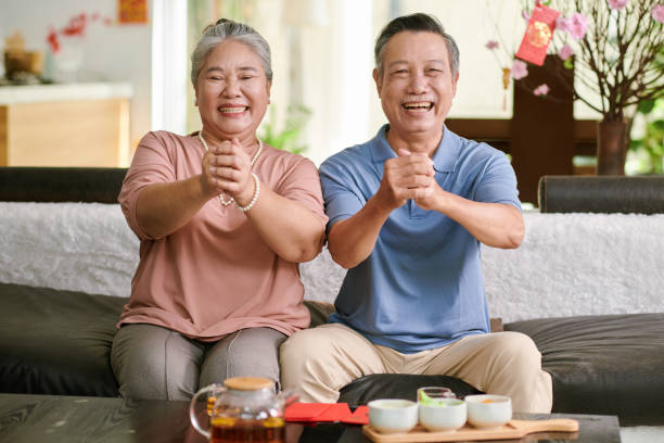 Senior Couple Making Greeting Gesture Happy senior man and woman making greeting gesture and smiling at camera vietnamese old man portrait stock pictures, royalty-free photos & images