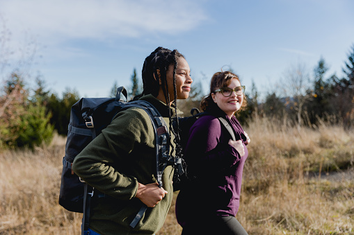 A multi racial mom and daughter bond together as they hike through a nature park together on a bright winter day. Shot with clear sky and copy space. They use their cell phone to take photos and selfies to document the day spent together.