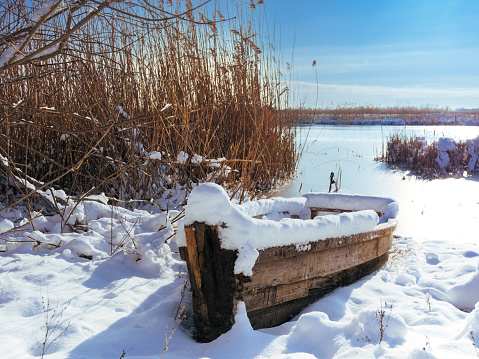 a wooden boat covered with snow on the background of a frozen river. winter river is covered with snow. ice on the river. old boat fucking river covered with snow.