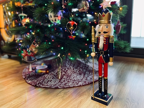 a toy soldier wooden nutcracker statue standing in front of decorated Christmas tree