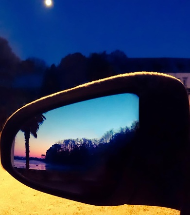 High contrast photo taken at dawn in winter in freezing weather. \nPhoto taken reflected in a car mirror surrounded by frost. \nFrom the front, the night and the moon. \nIn the reflection of the rearview mirror, the beach of Kerleven lit by city lights. \nPalm tree, sea and forest at the rendezvous.