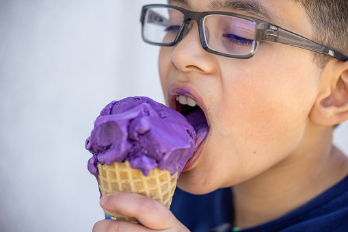 High quality stock photo of a Asian American mixed race boy eating ube ice cream on a hot day.