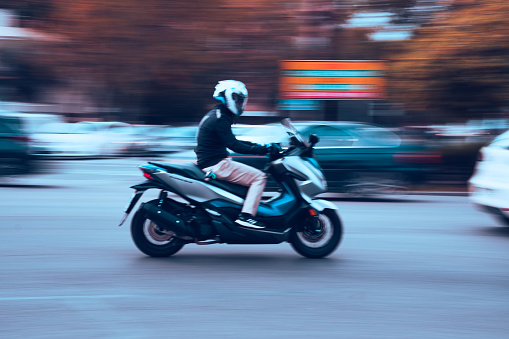 Seville, Spain; December 6th 2022: Motorcyclist on a 125cc scooter speeding through the city. Motorbike riding in the city as a concept of speed. Motion image