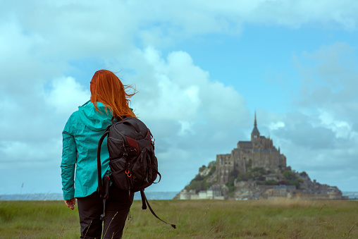 Rear view of redhead Backpacking woman looking at Mont Saint Michel in the distance