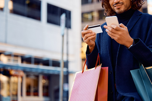 Primer plano del hombre usando el teléfono celular y la tarjeta de crédito mientras compra en la ciudad. photo