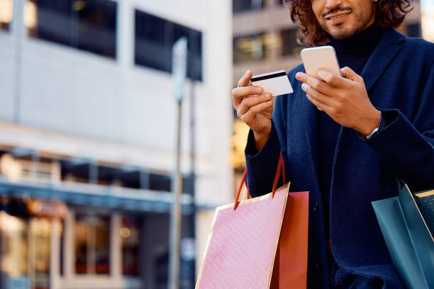 Close up of man using cell phone and credit card while shopping in the city. Close up of man checking his bank account with credit card and smart phone after shopping day in the city. shopaholic stock pictures, royalty-free photos & images