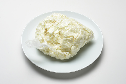 Goat cheese in a transparent plastic bag on the plate and white background. Turkish food Tulum cheese