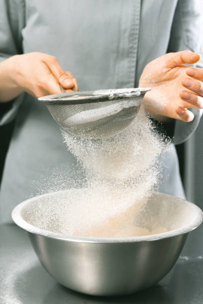 Vertical shot of some hands of a female chef sieves some white flour. stock photo