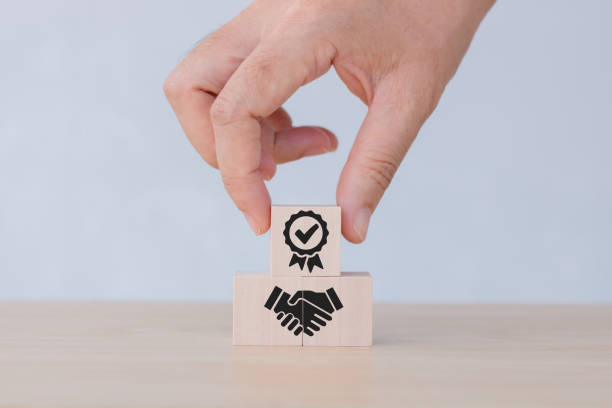 istock ISO certification and standardization concept. Wooden cube blocks with hand holding standard quality symbol on grey background. Certification, quality management, assurance for industry. 1449449985