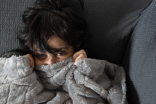 mature woman of Middle Eastern ethnicity covered with blanket on the sofa at home in cold winter. expression of happiness and tenderness on her face.