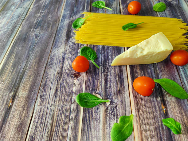 Spaghetti, cherry tomatoes, parmesan and spinach leaves on a wooden table. Essential Ingredients for Italian Pasta. Place for signature