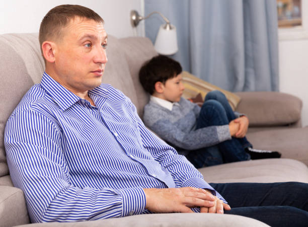 istock Upset father sitting after quarrel at home, son on background 1449459207