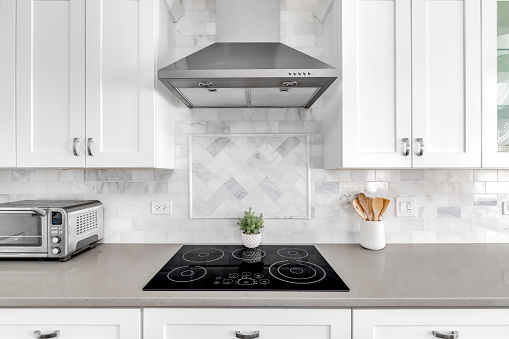 Detail shot of a white luxurious kitchen stove and hood. A marble custom tile back splash is under the white cabinets.