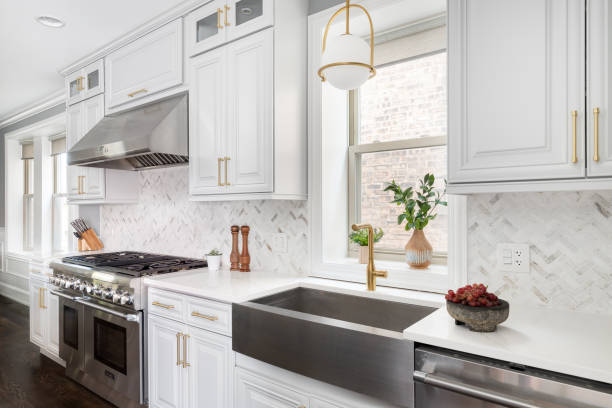 A beautiful kitchen with grey cabinets and stainless steel appliances. A luxurious white and grey kitchen with a large island, stainless steel Thermador appliances, and gold hardware, lights, and faucet. cupboard stock pictures, royalty-free photos & images