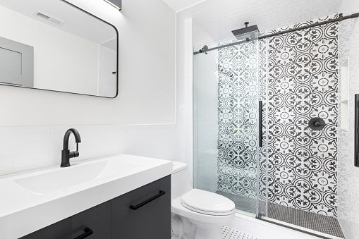 A bathroom with a grey vanity cabinet, white sink, and a black and white pattern tile shower.