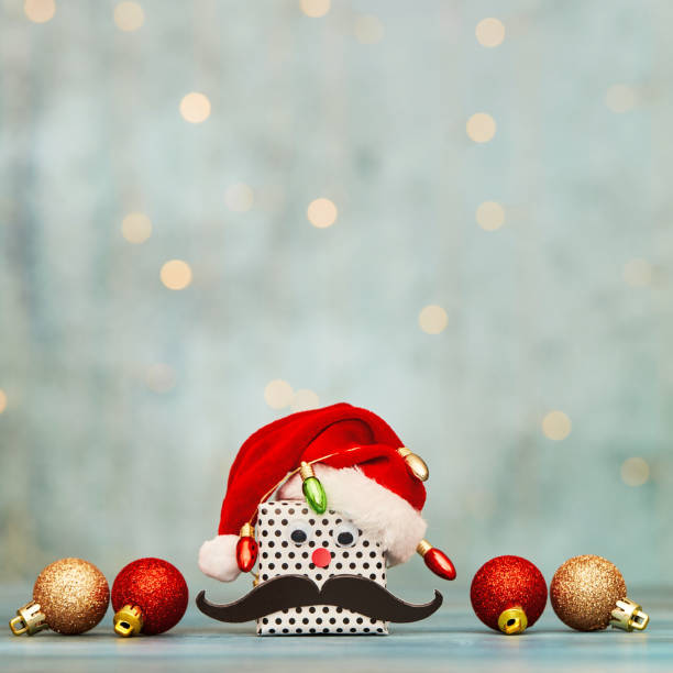 Cute Christmas gift wearing a Santa hat wrapped in tiny Christmas lights. Background with ornaments and copy space