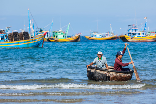 Phan Thiet, Vietnam - 5 June, 2011: Two fishermen in a coracle boat returning from fishing. Phan Thiet is a coastal city famous for its tourism district Mui Ne and seafood as well as sea products.