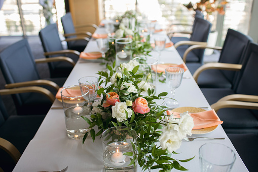 The table is set in a restaurant with a beautiful decor. The long banquet table is decorated with flowers and floating candles. On the eve of the wedding party