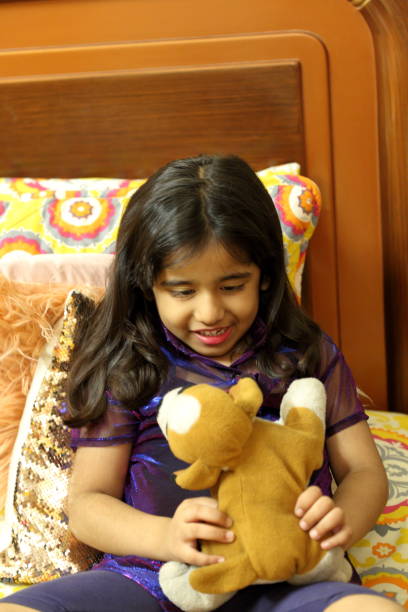 a little girl giving toothy smile and playing with her stuffed puppy toy in her bedroom. - offspring child toothy smile beautiful imagens e fotografias de stock