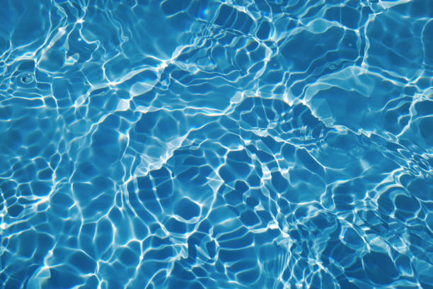 Defocus blurred transparent blue colored clear calm water surface texture with splashes and bubbles. Trendy abstract nature background. Water waves in sunlight with caustics. Blue water shinning