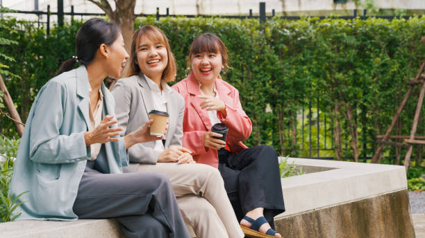 istock Young Asian businesspeople startup company team study work together share cafe table talking laughing at funny joke in park. 1449504396