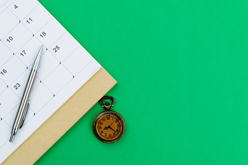Calendar and pocket watch on green background.