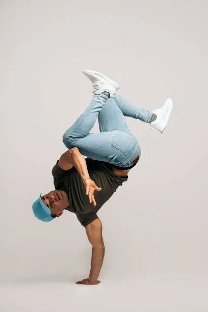 Hispanic dancer with casual clothes doing handstand and dancing in studio shot against white background.