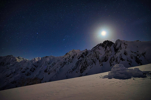 The starry sky with the shining moon and the snow-capped Mt. Goryu in the Japan Alps