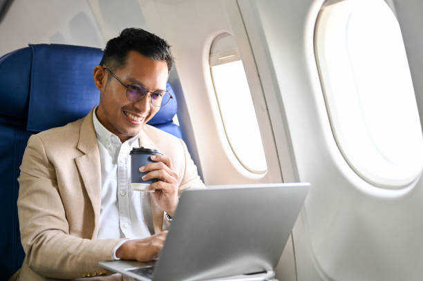 Smart Asian businessman sipping coffee, using a laptop to manage his tasks during the flight. Smart and professional Asian businessman or male CEO sipping coffee, using a laptop computer to manage his business tasks during the flight. private jet plane stock pictures, royalty-free photos & images