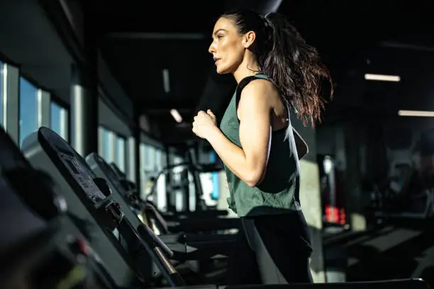 Young female athlete jogging on treadmill during sports training in a gym.