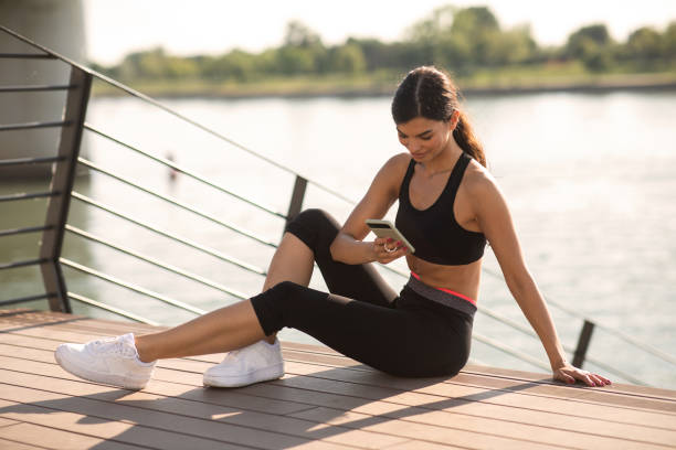 istock Young happy female athlete sitting while typing message on her smart phone outdoor 1449531994