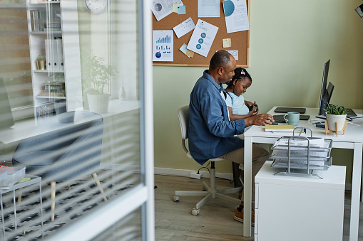 Side view portrait of black father with daughter working in office setting, bring child to work day, copy space