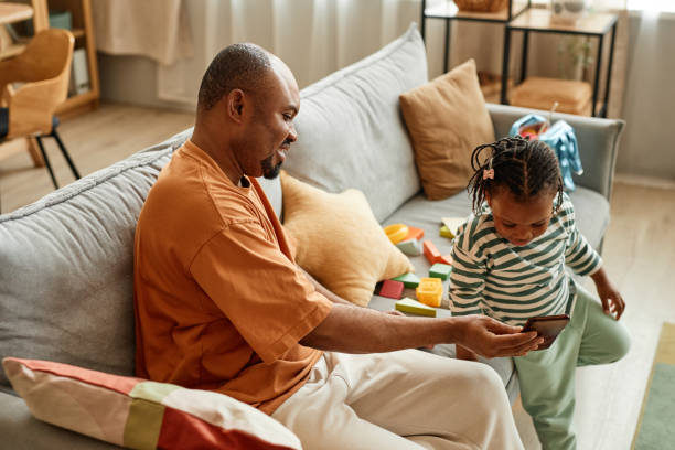 Happy black father showing smartphone to cute daughter