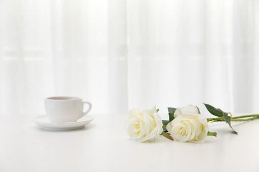 The two white roses and a cup of coffee on the table on a white background