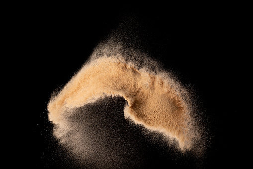 Small size fine Sand flying explosion, Golden grain wave explode. Abstract cloud fly. Yellow colored sand splash silica in Air. Black background Isolated high speed shutter, throwing freeze shot