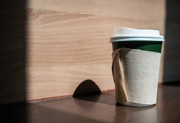 Photo of A paper cup of hot drink on wooden table.