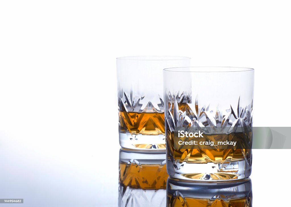 Two half-full glasses of whisky on a white background Two Glasses  of Whisky on a Reflective Surface with Copy Space Alcohol - Drink Stock Photo