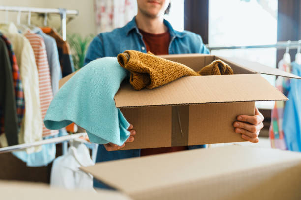 Pre owned clothes resale or donation. Man holding box with clothes, concept of clothes donation clothing swap photos stock pictures, royalty-free photos & images