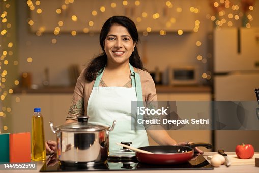 istock Portrait of Indian woman enjoying while cooking meal in the kitchen. stock photo 1449552590