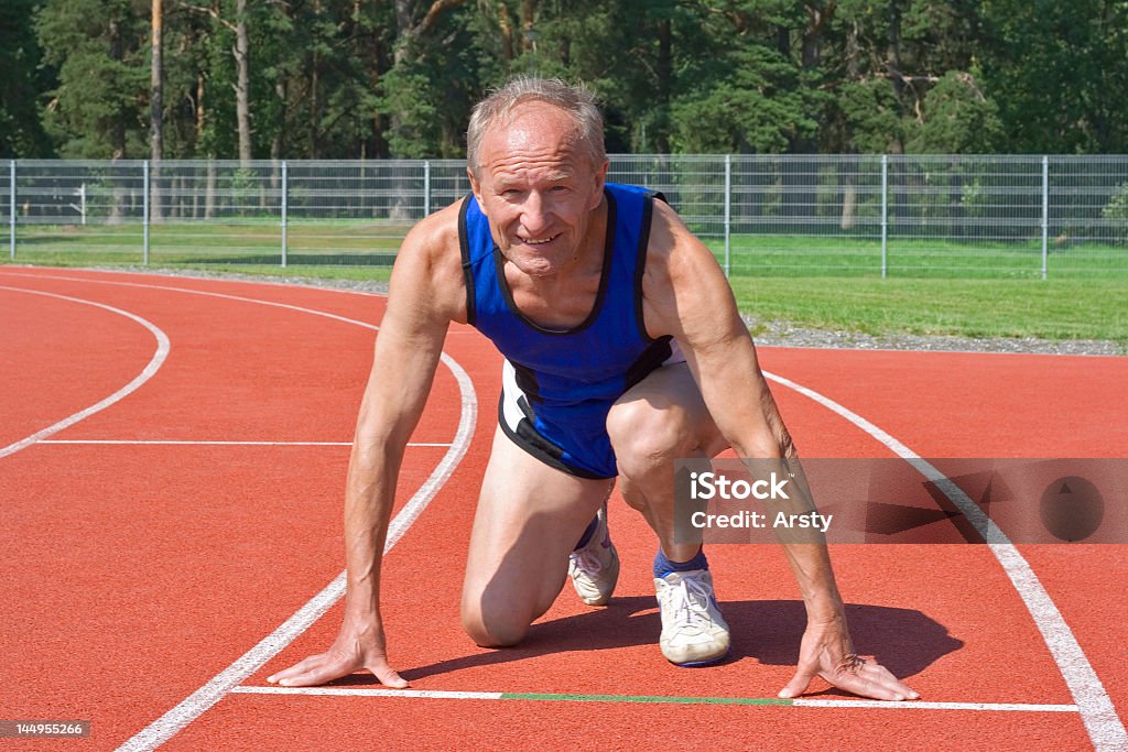 Senior male in the starting position to run on a track Senior runner in starting position on track Muscular Build Stock Photo