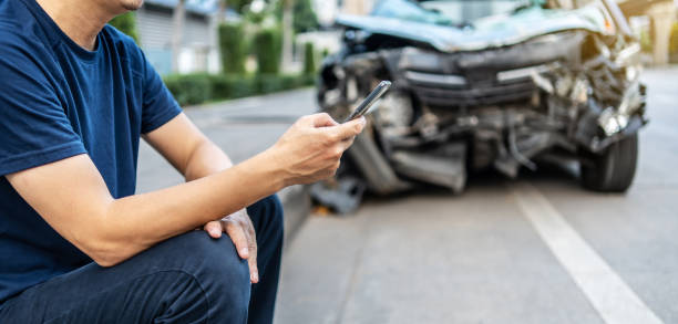 uomo che chiama con il telefono al suo agente assicurativo dopo incidente stradale con uno sfondo dell'auto incidentata, assicurazione auto un concetto di assicurazione non vita. - roadside emergency foto e immagini stock