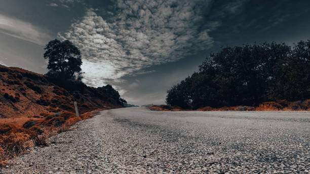 vista del cielo, los árboles, los maquis y las nubes a lo largo de una carretera asfaltada desgastada en una ciudad del egeo - country road lane road dirt road fotografías e imágenes de stock