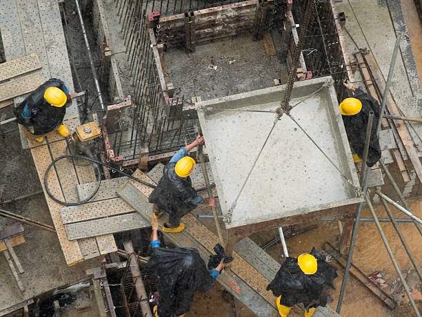 Yellow Hard Hats Construction workers in yellow hard hats directing a cement bucket to its location in the pouring rain crane machinery stock pictures, royalty-free photos & images