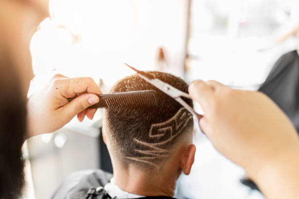 istock Barber shaving designs into a clients hair holding scissors 1449561652